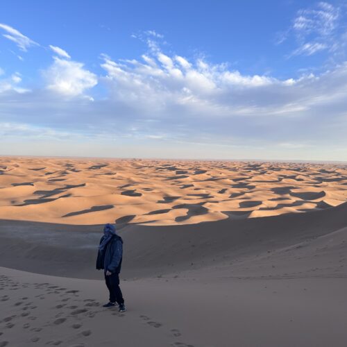Randonneur face aux dunes du Sahara marocain au lever du soleil